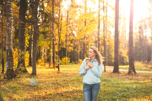 Foto een mooie, gelukkige blonde vrouw loopt door het herfstpark met een kopje verwarmende drank in haar