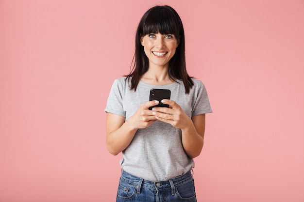 een mooie geweldige opgewonden gelukkige vrouw poseren geïsoleerd over licht roze muur muur met behulp van mobiele telefoon.