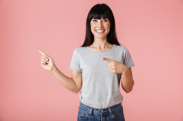 Een mooie geweldige vrouw poseren geïsoleerd over licht roze muur muur wijzen.