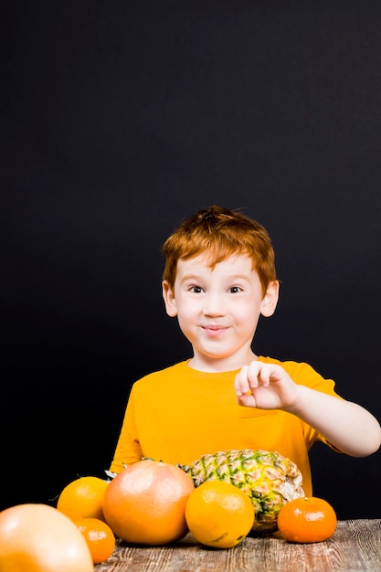 een mooie gezellige roodharige jongen met citrusvruchten waar je sap of ander eten van kunt maken, de jongen eet en speelt graag met citrusvruchten op tafel