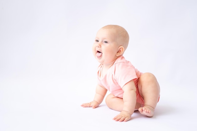 Een mooie, gezonde, vrolijke baby in een roze bodysuit zit op een witte achtergrond, het kind lacht isolaat