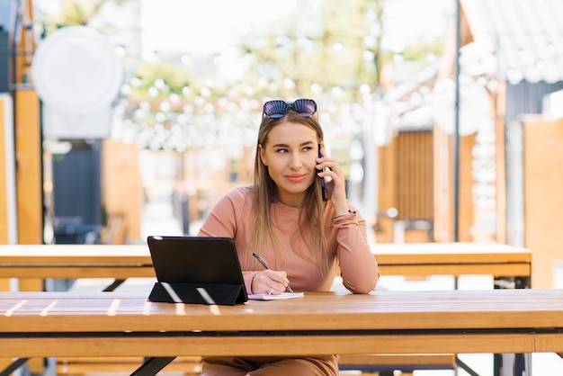 Een mooie glimlachende zakenvrouw met een smartphone in haar handen zit op haar werkplek