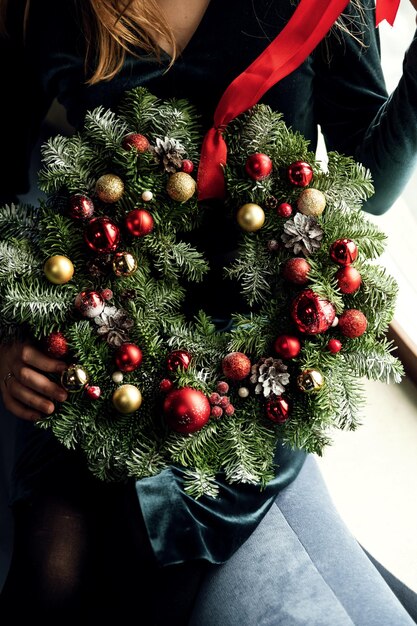 Een mooie groene kerstkrans versierd met een bal en een lint wordt vastgehouden door een meisje in haar handen. nieuwjaar vakantie. krans voor feest.