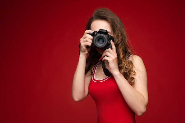 Een mooie heldere vrouw met een camera in haar handen Een vrouw op een rode achtergrond in een rood zwempak poseert met een camera