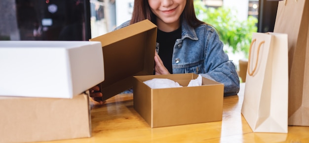 Een mooie jonge Aziatische vrouw die een postpakketdoos ontvangen en openen thuis in zakken doen voor levering en online het winkelen concept