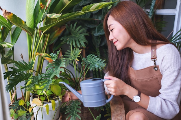 Een mooie jonge aziatische vrouw die kamerplanten verzorgt en water geeft door thuis een gieter te geven