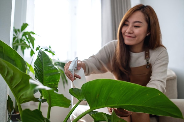 Een mooie jonge aziatische vrouw die kamerplanten verzorgt en water geeft met een spuitfles thuis