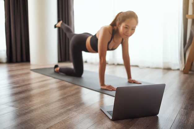 Een mooie jonge aziatische vrouw die thuis naar online workout-tutorials op laptop kijkt