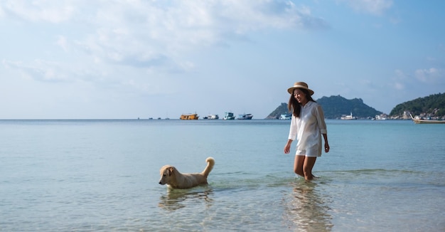 Een mooie jonge Aziatische vrouw en een hond die samen in de zee spelen