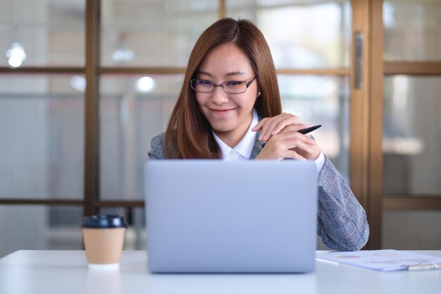 Een mooie jonge Aziatische zakenvrouw die een laptop gebruikt terwijl ze op kantoor werkt