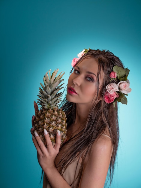 Een mooie jonge brunette met helderblauwe ogen in een hawaiiaans beeld met ananas in handen nat ha...