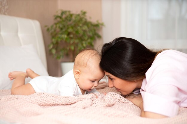 Een mooie jonge moeder speelt en knuffelt met haar baby op het bed Love motherhood Lifestyle