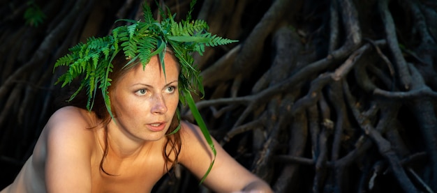 Een mooie jonge naakte vrouw met een varenkrans op haar hoofd genietend van de natuur in de bosrivier