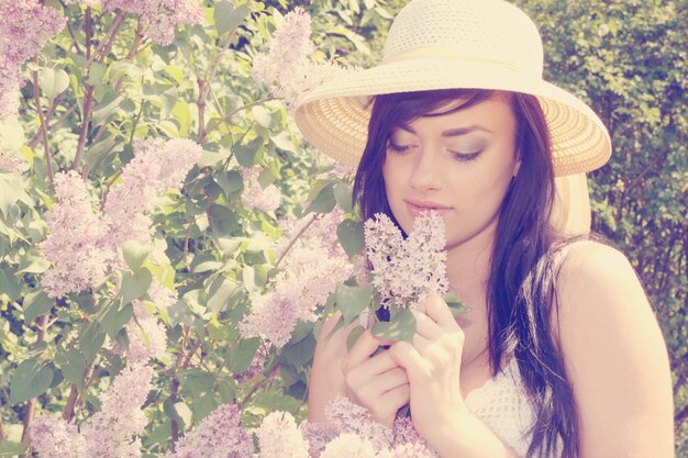 Een mooie jonge vrouw die een bloeiende lila struik ruikt