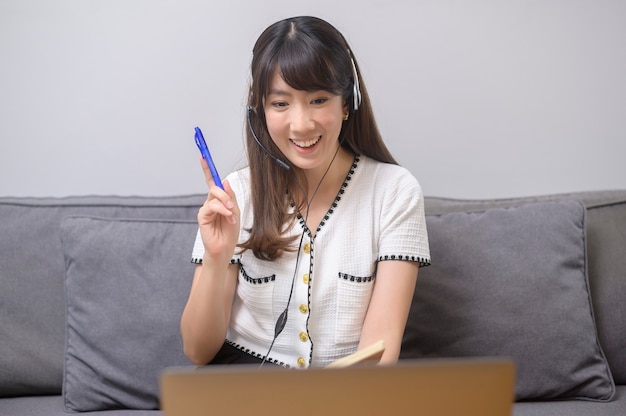 Een mooie jonge vrouw die een hoofdtelefoon draagt, voert thuis een videoconferentiegesprek via de computer