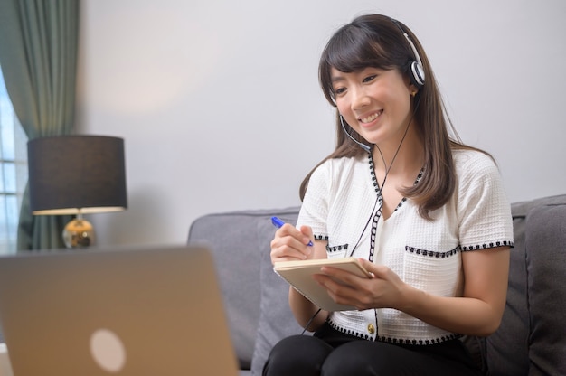 Een mooie jonge vrouw die een hoofdtelefoon draagt, voert thuis een videoconferentiegesprek via de computer