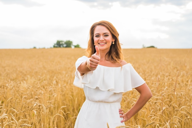 Een mooie jonge vrouw die je een duim omhoog geeft en lacht in een veld met een blauwe lucht.