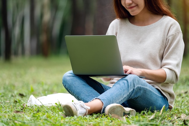 Een mooie jonge vrouw die op het toetsenbord van de laptop werkt en typt terwijl ze in het park zit