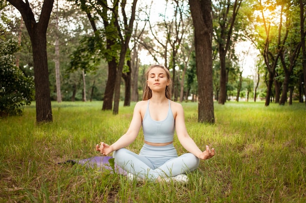 Een mooie jonge vrouw die yoga doet in het park op het gras. Gymnastiekmat, sportuitrusting. Training, openlucht. Gezonde levensstijl, gewichtsverlies, fitness. Getraind gespierd lichaam. Verse lucht. zonnige schittering