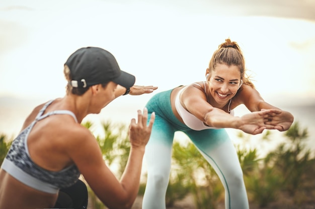 Foto een mooie jonge vrouw doet rekoefeningen op het zeestrand in een zonnige zomerdag, ondersteund door haar vrouwelijke personal trainer.