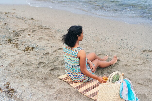 Een mooie jonge vrouw drinkt wijn op het strand, kijkend naar de horizon.