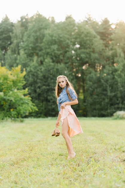 Een mooie jonge vrouw houdt zomerschoenen in haar handen en loopt op een zomerdag blootsvoets op het gras