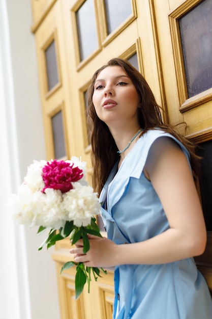 Een mooie jonge vrouw in een blauwe jurk met een boeket pioenrozen