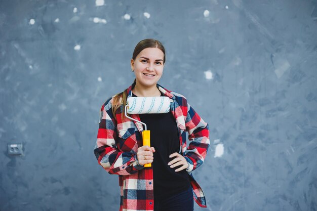 Een mooie jonge vrouw in een geruit hemd renoveert haar kamer met een verfroller