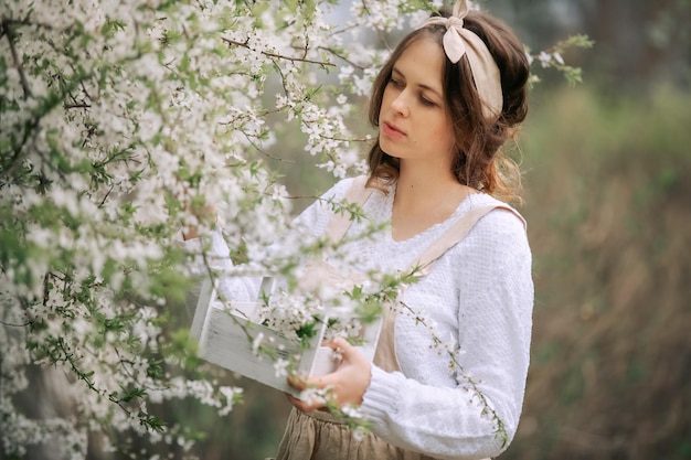 Foto een mooie jonge vrouw in het schort geniet van het leven in een bloeiende lentetuin met bloesem