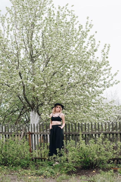 Een mooie jonge vrouw in zwarte kleding en een hoed in een bloeiende tuin in het voorjaar 1