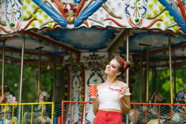 Een mooie jonge vrouw loopt in een pretpark en houdt een papieren beker in haar handen