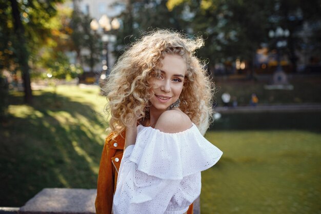 Een mooie jonge vrouw met blond krullend haar loopt door de zonnige stad, geniet van een lunchwandeling