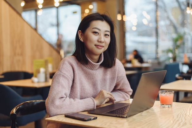 Een mooie jonge vrouw met een aziatische uitstraling werkt aan een laptop in een café. concept van werk buitenshuis, freelance.