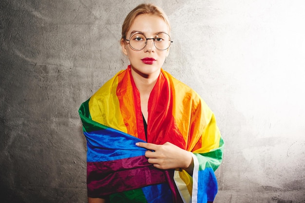 Een mooie jonge vrouw met een ronde bril en een regenboog LGBTQ-vlag. Lesbisch, homoseksueel, biseksueel, transgender, queer. homoseksuele man