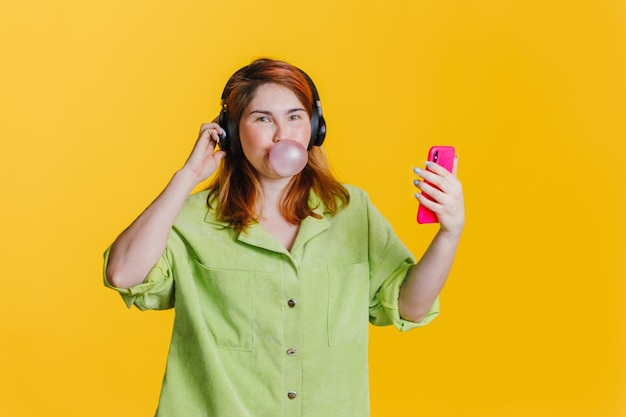 Een mooie jonge vrouw met rood haar die muziek in de koptelefoon luistert en een kauwgombal opblaast