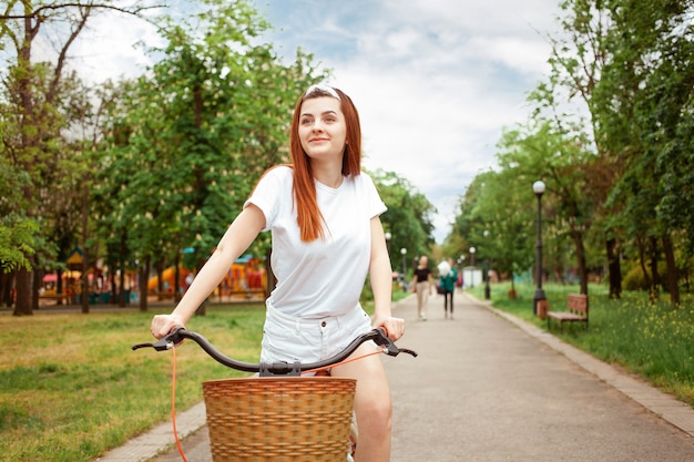 Een mooie jonge vrouw rijdt op haar fiets in het park. Huur vervoer voor een dag. Zomer lente. Het gelukkige meisje glimlacht. Sport gezonde levensstijl, buiten.