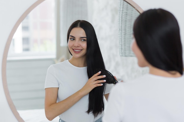 Een mooie jonge vrouw staat en kijkt naar zichzelf in de spiegel, ze kamt haar haar met een borstel