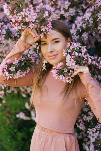 Een mooie jonge vrouw staat in het voorjaar naast een decoratieve bloeiende roze appelboom