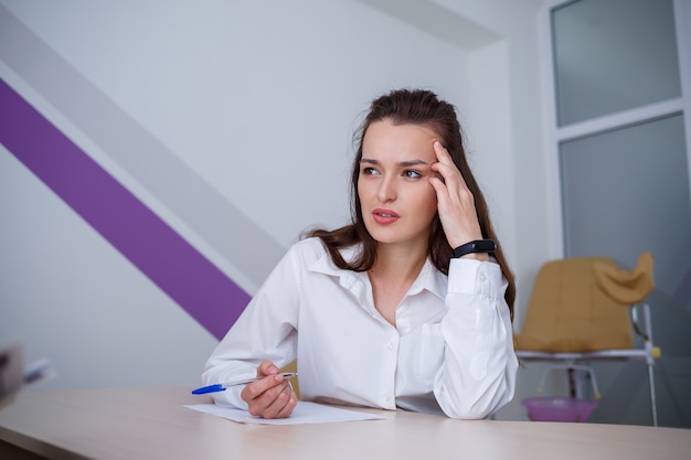 Een mooie jonge vrouw zit aan een tafel en ondertekent belangrijke documenten.