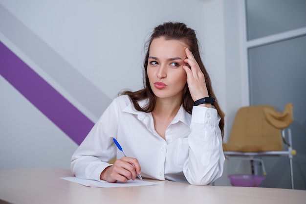 Een mooie jonge vrouw zit aan een tafel en ondertekent belangrijke documenten.