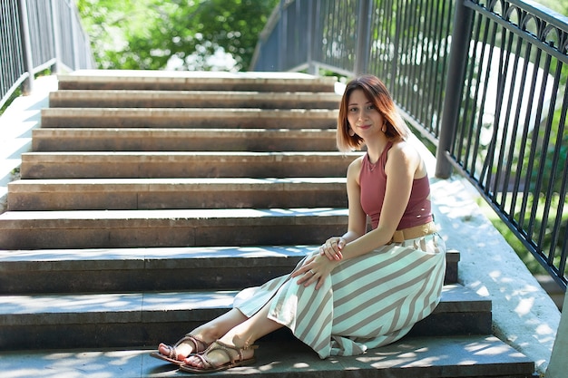 Een mooie jonge vrouw zit op de trappen van een brug op een zomerse dag.