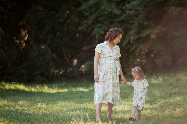 Een mooie jonge zwangere moeder en haar dochtertje plukken bloemen in een veld. moederschap. een familie. zomer.