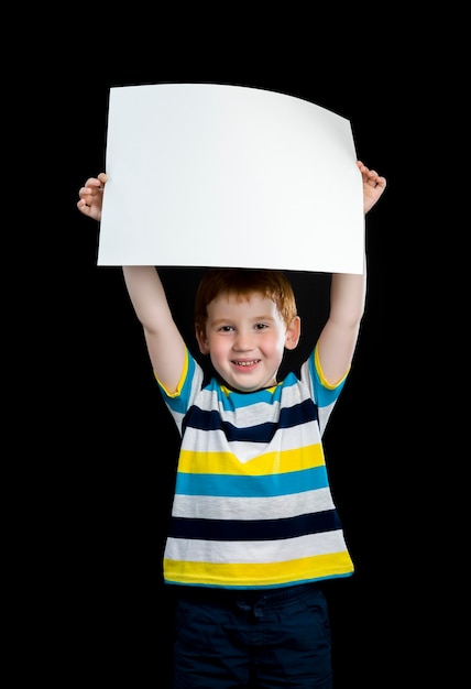 Een mooie jongen heeft een groot vel schoon wit papier in zijn handen, een close-upportret van een schattig roodharig kind