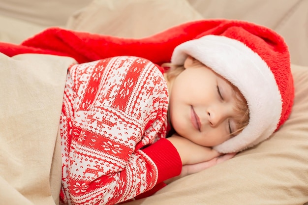 een mooie jongen in nieuwjaarspyjama en een kerstmuts ligt in bed