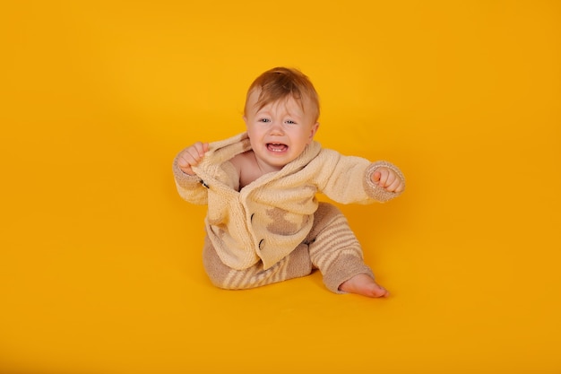 een mooie kleine jongen met blauwe ogen in een gebreid beige warm pak op een gele achtergrond