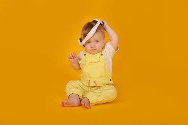 een mooie kleine jongen met blauwe ogen in een geel pak zit in een witte koptelefoon