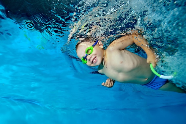 Een mooie kleine jongen zwemt onder water in het zwembad en kijkt ernaar uit en glimlacht