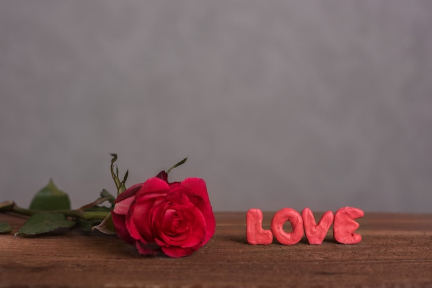 Een mooie knop van een bloeiende roos en het opschrift "love" gemaakt van volumineuze letters op een houten ondergrond. Een kaart voor Lovers' Day. Romantische compositie.