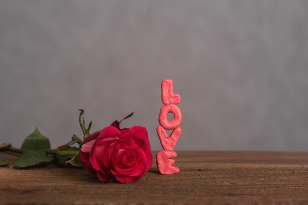 Een mooie knop van een bloeiende roos en het opschrift "love" gemaakt van volumineuze letters op een houten ondergrond. Een kaart voor Lovers' Day. Romantische compositie.