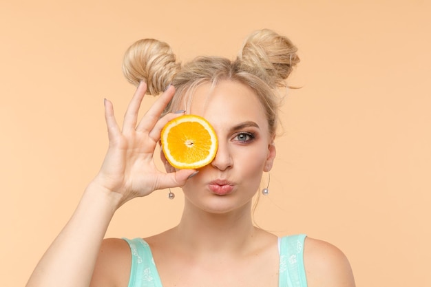 Een mooie lieve charmante frisse, heldere vrouw met een cool kapsel houdt 2 sinaasappelschijfjes in haar handen zomervreugde helderheid kopieerruimte voor reclame